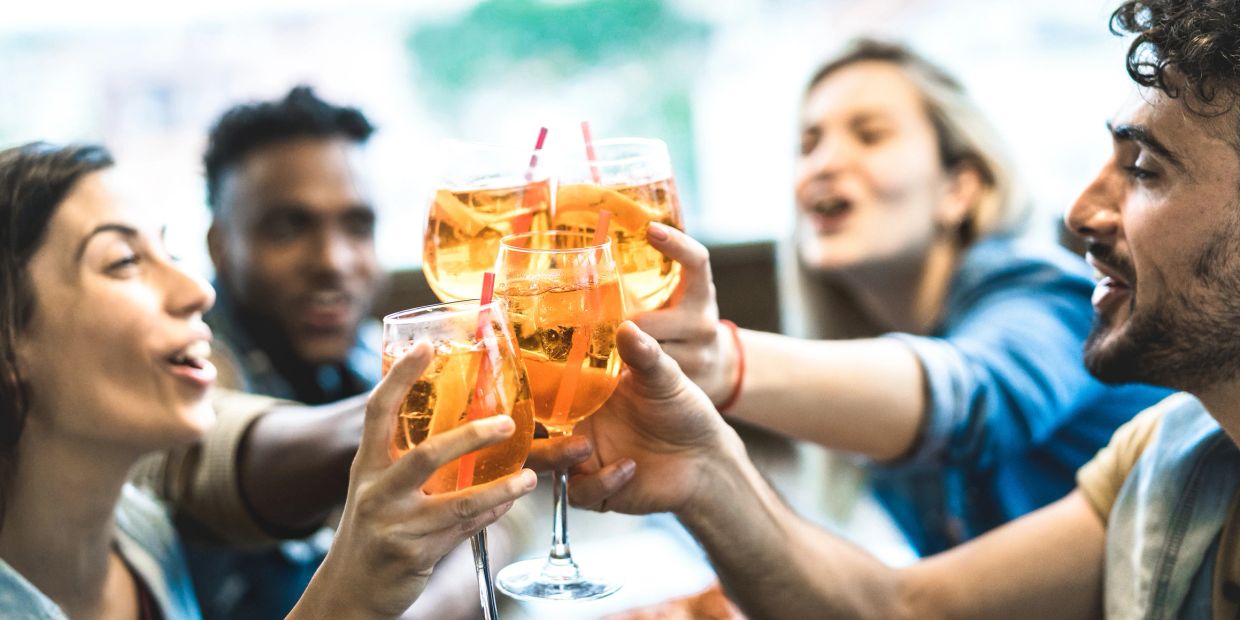 Friends clinking glasses with orange drinks, celebrating together.