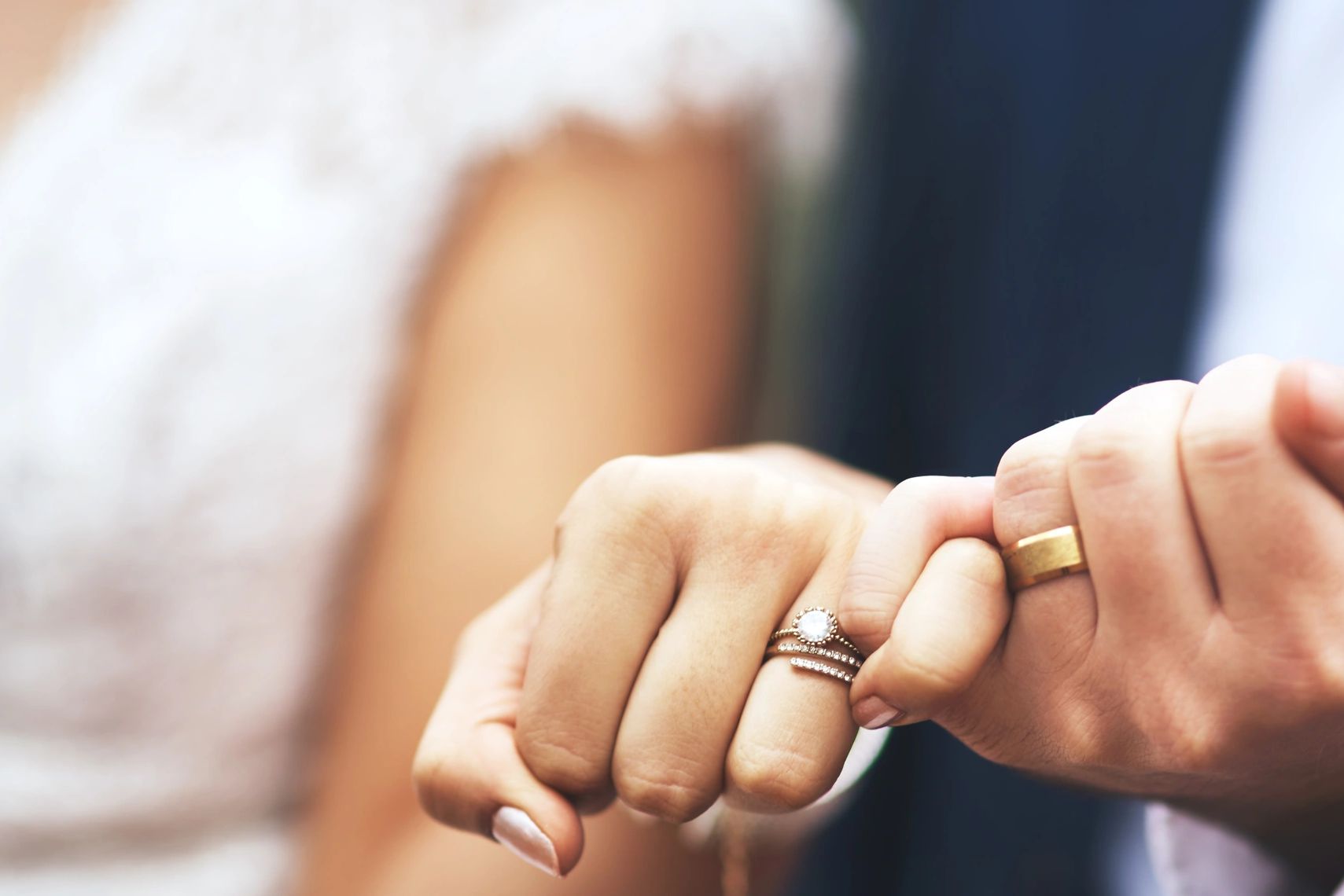 A newlywed couple linking pinky fingers, showing wedding rings.