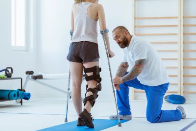 Physical therapist assisting a woman with leg injury on crutches.