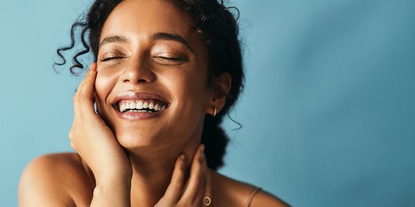 Joyful woman with eyes closed smiling against a blue background.