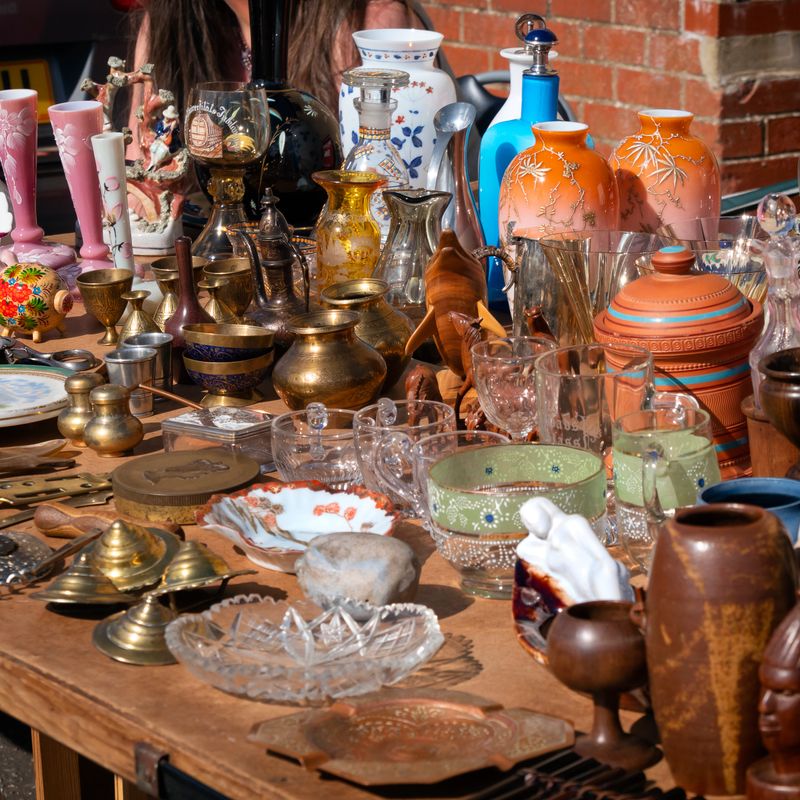 A display of vintage and antique items on an antiques market stall on a sunny day, including vases, dishes, bowls, brass, glass, china and earthenware.