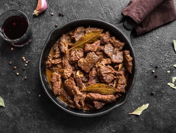 Cooked beef stew with bay leaves in a cast iron skillet.