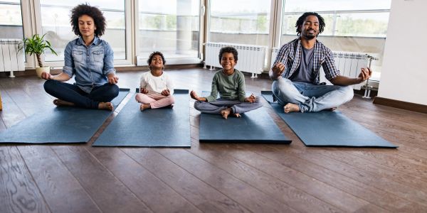 Family of four meditating on yoga mats indoors.