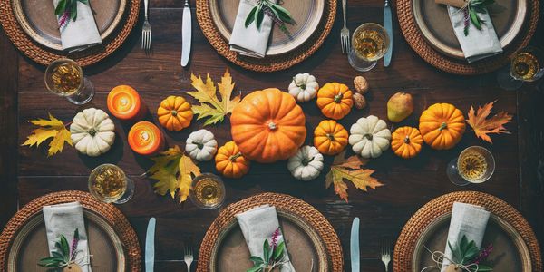 A rustic fall-themed dining table with pumpkins, leaves, candles, and elegant place settings.
