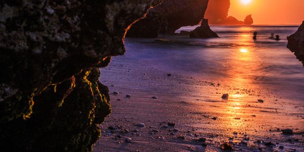 Sunset over a rocky beach with reflections on wet sand.