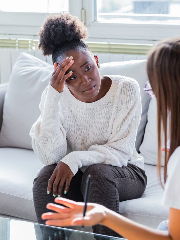 A woman in distress talks to a therapist in a bright room.
