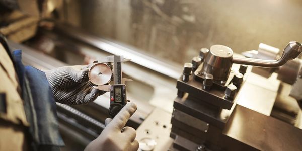 Precision machining measurement using digital calipers on a custom metal component.