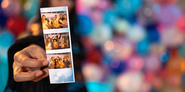 Person holding a photo strip with friends at a colorful party.
