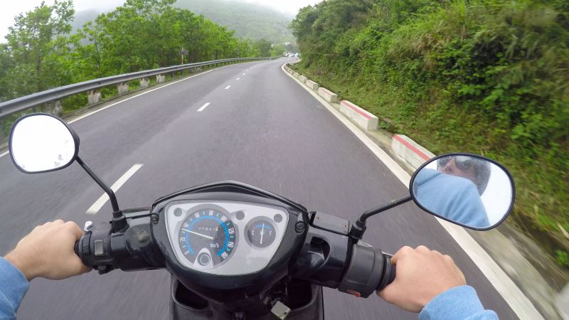POV: Riding a motorcycle along empty asphalt road leading through the tropical forest in picturesque Vietnam. Cool shot of riding a motorbike across the world famous scenic Hai Van mountain pass.