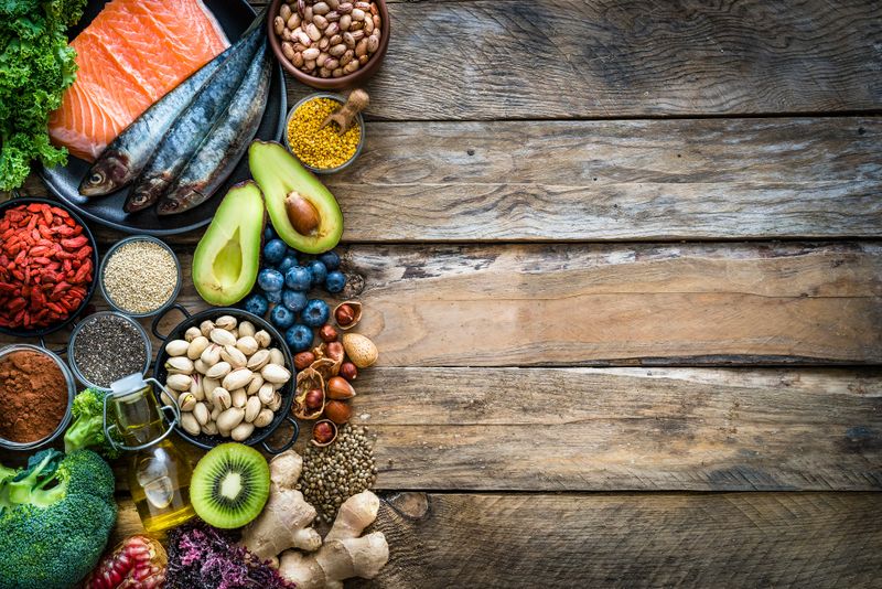 Top view of healthy, antioxidant group of food placed at the left border of a wooden table leaving useful copy space for text and/or logo at the center right. The composition includes food rich in antioxidants considered as a super-food like avocado, kale, blueberries, chia seeds, broccoli, different nuts, salmon, sardines, pollen, quinoa, hemp seeds, seaweed, cocoa, olive oil, goji berries, kiwi fruit, pistachio, seaweed, pinto beans, pomegranate and ginger. XXXL 42Mp studio photo taken with SONY A7rII and Zeiss Batis 40mm F2.0 CF
