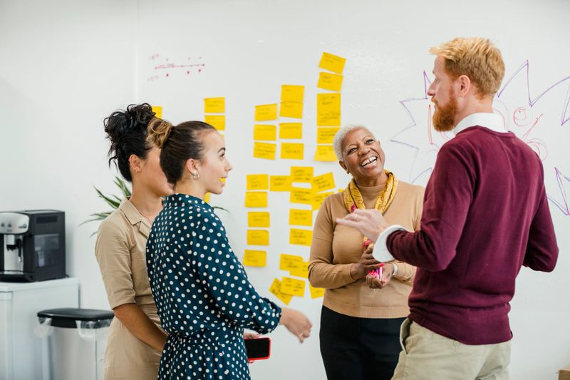 Colleagues standing in a small group discussing something and laughing while are standing in front of a whiteboard.