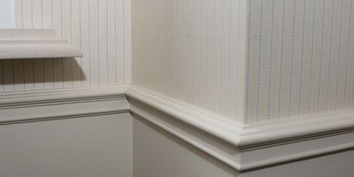 Close-up of room corner with beige wallpaper and white molding.