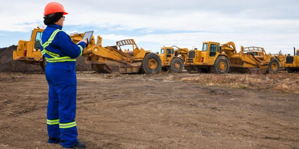 Construction worker in safety gear inspects heavy machinery at a worksite.