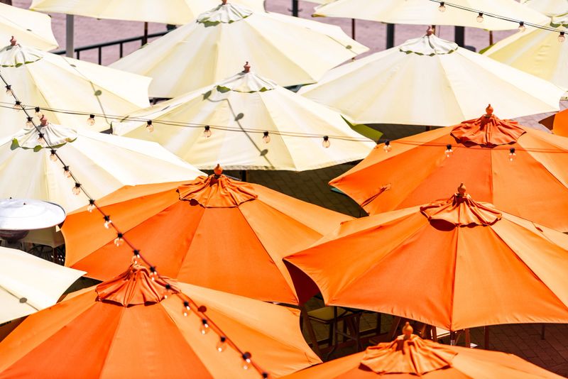 Many colorful yellow orange umbrellas high angle aerial bird's eye closeup view at cafe or restaurant in city during day with hanging light bulbs