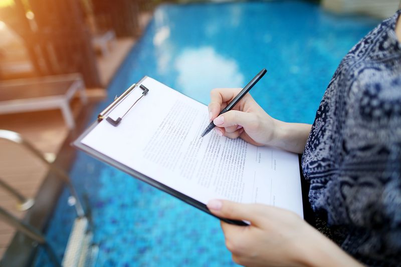 Photographed close hand of girl signing sunny day paper on pool background. concept of signing contract, travel, new contract or arrangement. Front used with Open Font License
