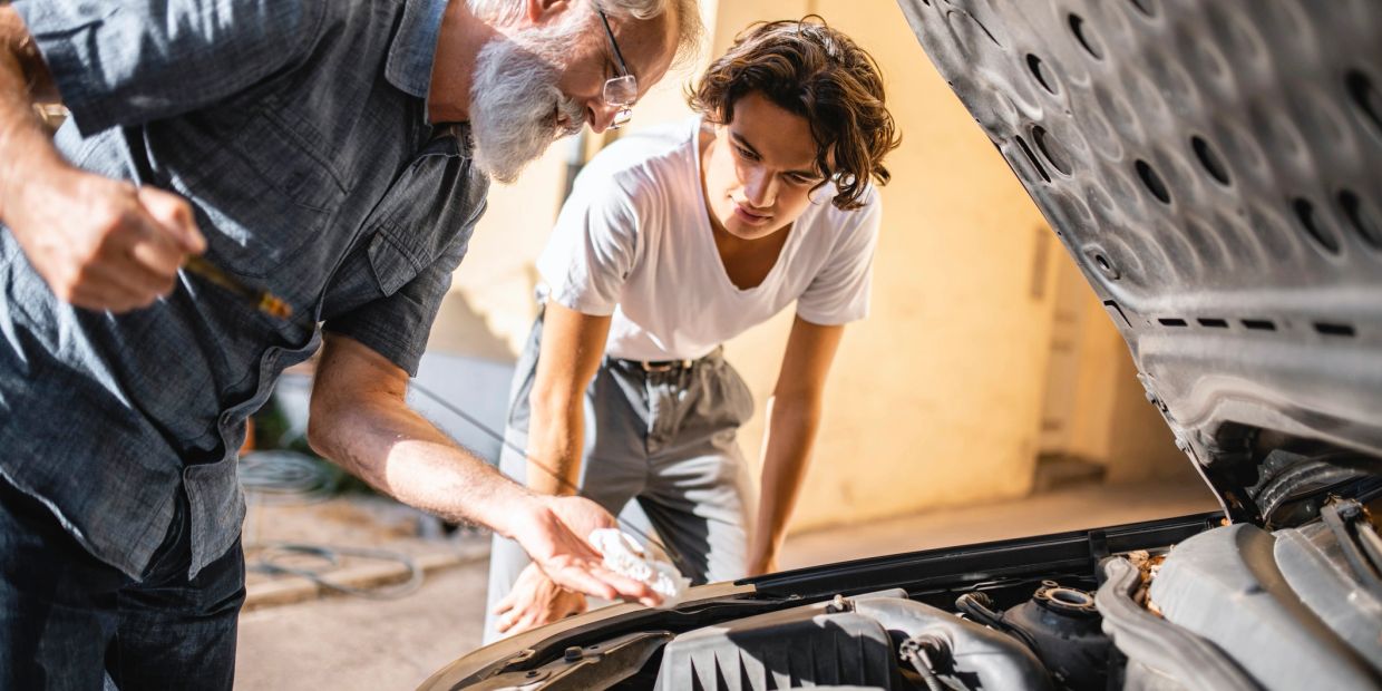 Hombre mayor enseñando reparación de coche a joven.