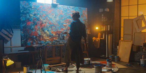 Artist painting a large abstract canvas in a cozy, dimly lit studio.