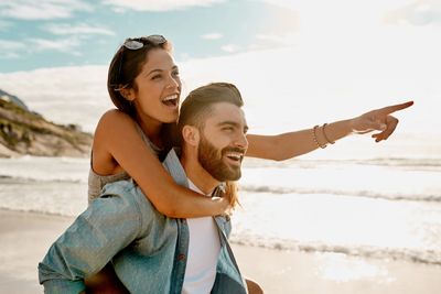 Happy couple enjoying a sunny day at the beach with the woman pointing at something.
