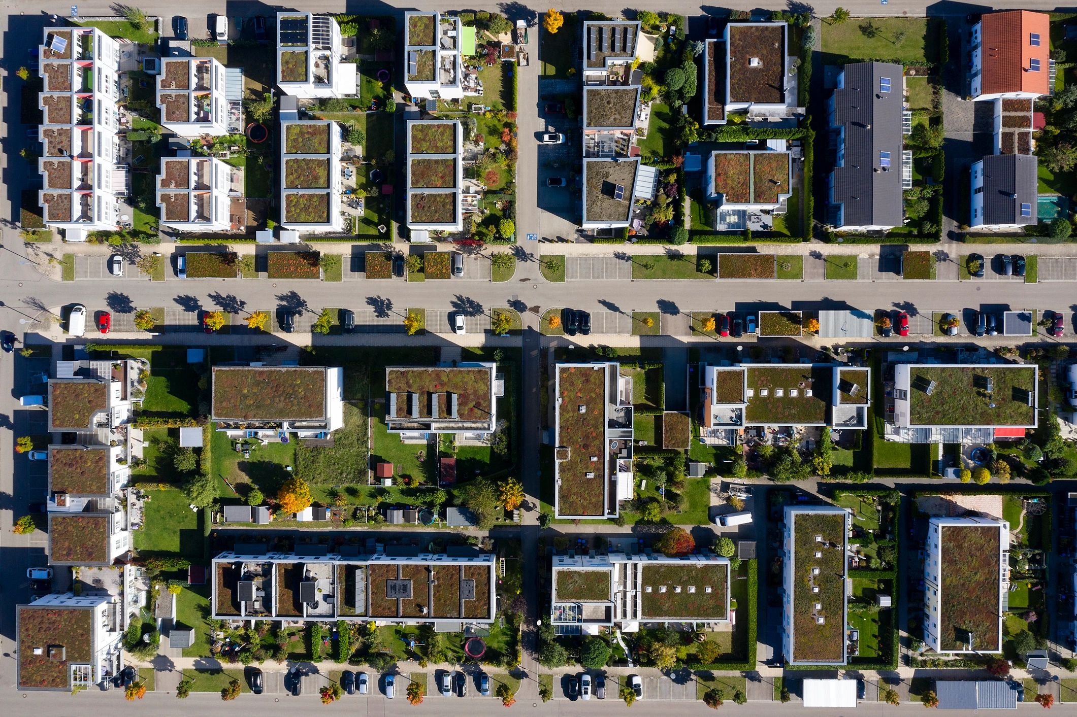 Aerial view of a residential area with green roofs and parked cars.