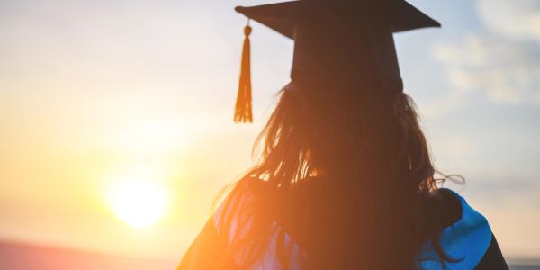 Graduate overlooking sunset celebrating achievement.