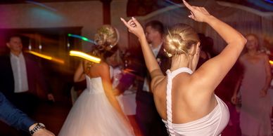 Women dancing at a lively wedding reception with colorful lights.