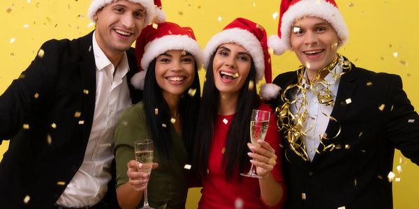 Four friends in Santa hats celebrating with champagne and confetti.