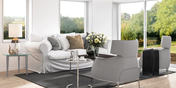 Bright modern living room with white sofa, gray chairs, and large windows.