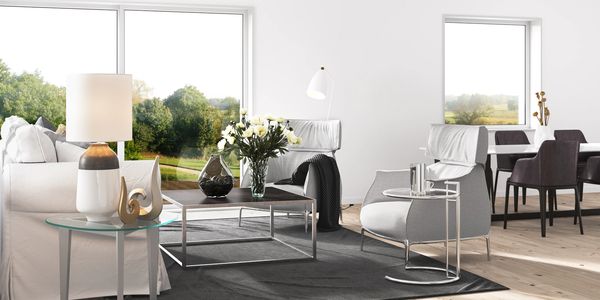 Bright modern living room with white furniture and large windows showing greenery.