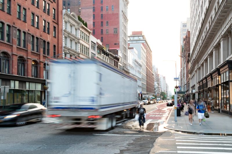 Busy view of 23rd Street with delivery truck speeding past the people walk down the sidewalk in Midtown Manhattan, New York City NYC