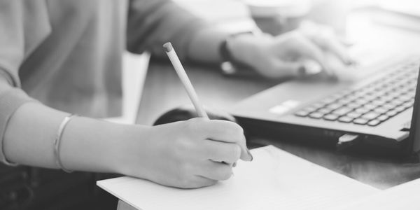 Person writing notes while using a laptop.