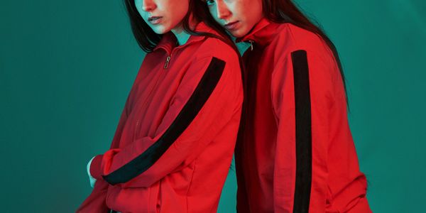 Two women in matching red jackets with black stripes posing against teal background.