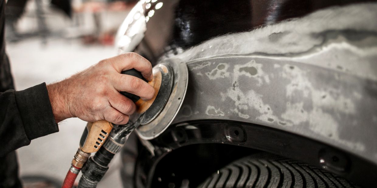 Hand sanding a car's body panel to prepare for painting.