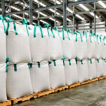 Rows of large white industrial bags stacked on pallets in a warehouse.