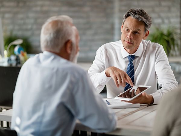 A businessman explaining something on a tablet to an elderly man.
