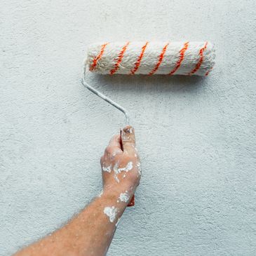 Hand holding a paint roller applying white paint on a wall.