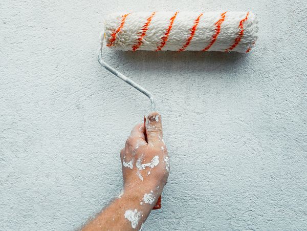 Hand holding a paint roller applying white paint on a textured wall.