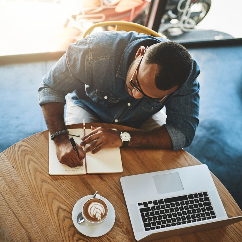 High angle shot of a handsome young businessman sitting alone in a cafe and writing in his notebook