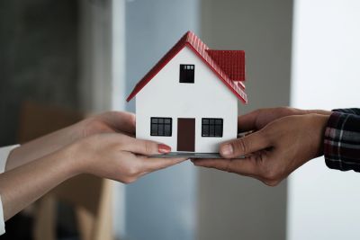 Hands exchanging a model house, representing property transfers and gifts of real estate in Ontario