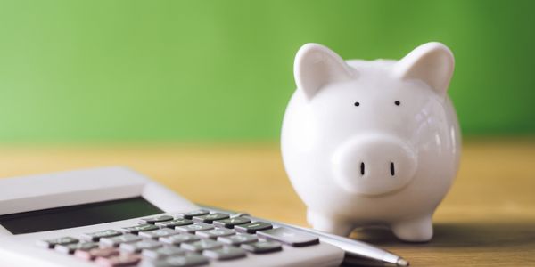 Small, white piggy bank next to a calculator.