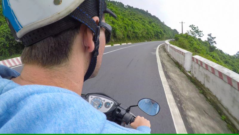 POV: Scenic view of the forest while sitting behind man riding the motorbike across the famous Hai Van pass. Adult male tourist enjoying a picturesque motorcycle ride through the spectacular mountains