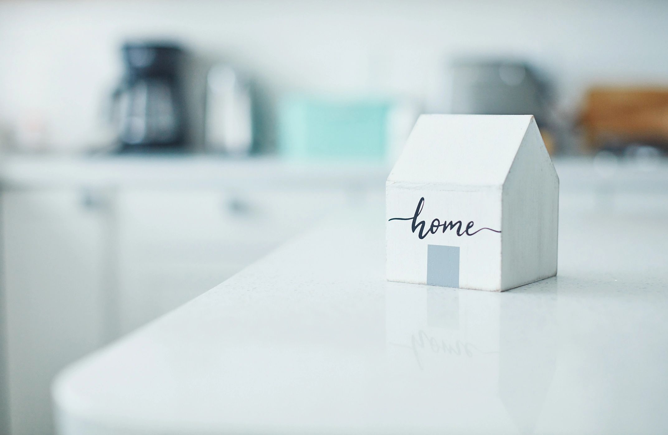 Small white house model with 'home' written on it on a clean kitchen counter.