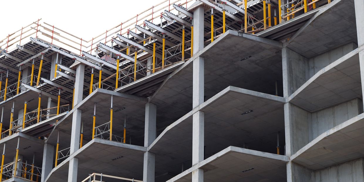 Concrete building under construction with yellow support beams and scaffolding.
