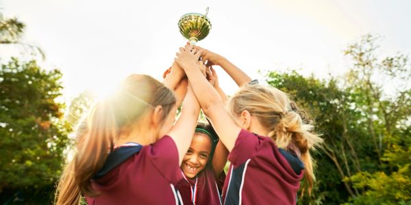 Young girls celebrating victory by holding a trophy outdoors.