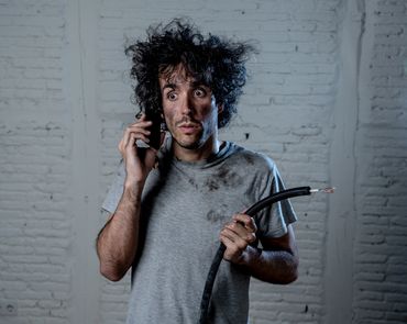 Surprised man with messy hair and dirty face holding wires and talking on phone.