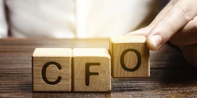Hand arranging wooden blocks spelling 'CFO' on a table.