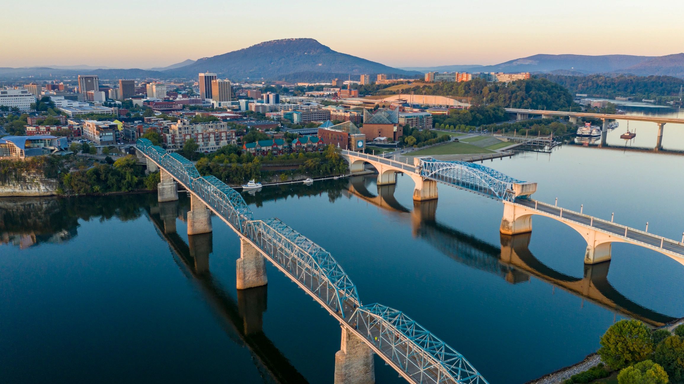View of city from above river at sunrise. Three bridges to town, with mountains behind city.