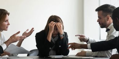A stressed woman being confronted by colleagues in a meeting.