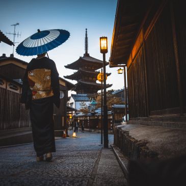 Person with umbrella walking towards a pagoda in traditional Japanese street.
