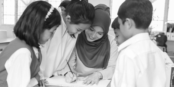 Teacher helping children with writing in a notebook.
