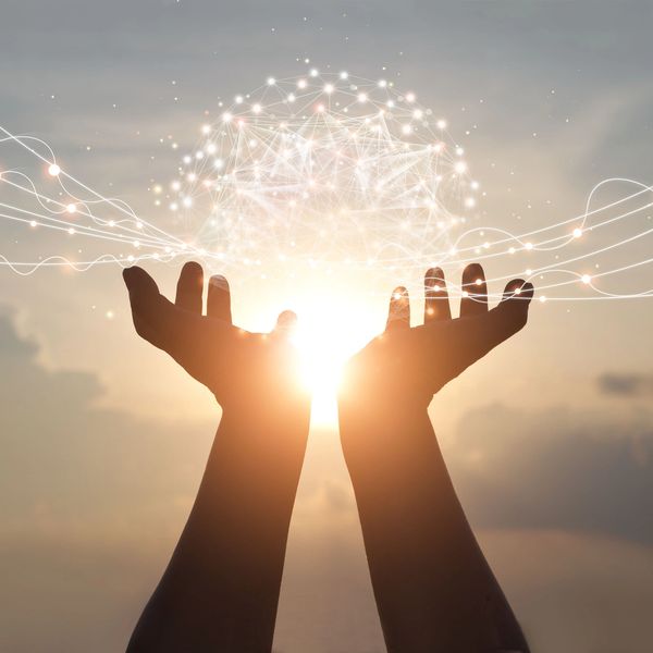 Hands holding a glowing network sphere with light trails at sunset.